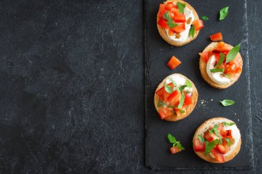 Doğranmış domates, fesleğen, mozzarella peyniri ve balsamik sirke ile İtalyan bruschetta. Taze ev yapımı caprese bruschetta veya crostini siyah taş zemin, kopya alanı üzerinde.