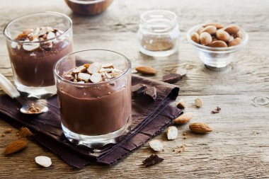 Çikolata Mousse ile badem ahşap arka plan üzerinde gözlük tepesinde yakın çekim - lezzetli ev yapımı çiğ Vegan çikolatalı puding ile fındık ve keçiboynuzu tozu