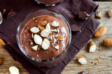 Çikolata Mousse ile badem ahşap arka plan üzerinde gözlük tepesinde yakın çekim - lezzetli ev yapımı çiğ Vegan çikolatalı puding ile fındık ve keçiboynuzu tozu