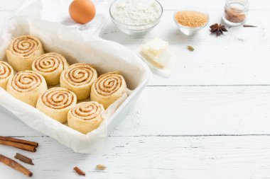 Rulo tarçın veya cinnabon, ev yapımı tarifi çiğ hamur hazırlık şekerli geleneksel tatlı çörek tepsisi beyaz arka plan, kopya alanı üzerinde pişirme üzerinde pasta malzemeler gıda ile.