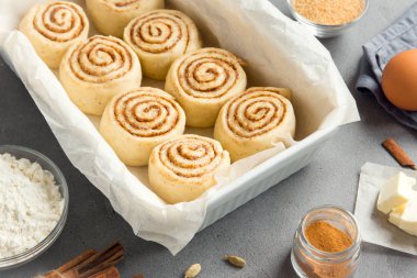 Rulo tarçın veya cinnabon, ev yapımı tarifi çiğ hamur hazırlık şekerli geleneksel tatlı çörek tepsisi üzerinde pişirme üzerinde pasta malzemeler gıda ile arka plan gri.