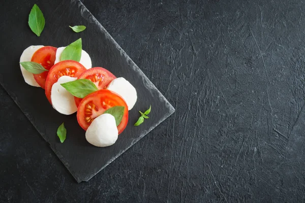 Geleneksel İtalyan Caprese salatası - dilimlenmiş domates, mozzarella peyniri ve fesleğen koyu taş arka plan, üstten görünüm, boşaltmak. Caprese salatası, İtalyan Akdeniz yemekleri.