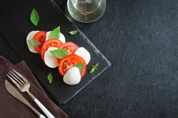 Geleneksel İtalyan Caprese salatası - dilimlenmiş domates, mozzarella peyniri ve fesleğen koyu taş arka plan, üstten görünüm, boşaltmak. Caprese salatası, İtalyan Akdeniz yemekleri.