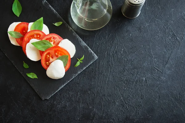 Geleneksel İtalyan Caprese salatası - dilimlenmiş domates, mozzarella peyniri ve fesleğen koyu taş arka plan, üstten görünüm, boşaltmak. Caprese salatası, İtalyan Akdeniz yemekleri.