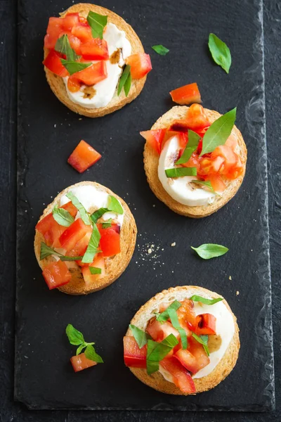 Doğranmış domates, fesleğen, mozzarella peyniri ve balsamik sirke ile İtalyan bruschetta. Taze ev yapımı caprese bruschetta veya crostini siyah taş zemin, kopya alanı üzerinde.