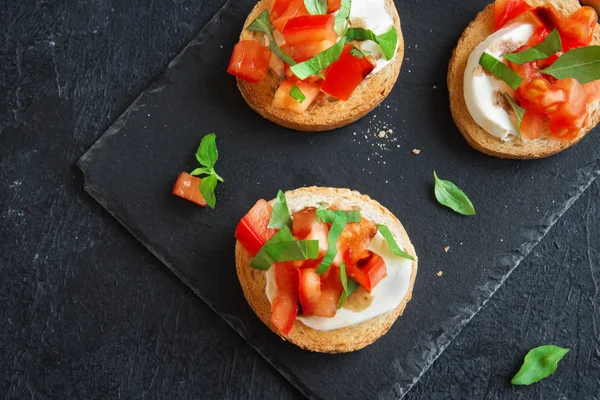 Doğranmış domates, fesleğen, mozzarella peyniri ve balsamik sirke ile İtalyan bruschetta. Taze ev yapımı caprese bruschetta veya crostini siyah taş zemin, kopya alanı üzerinde.