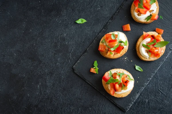 Doğranmış domates, fesleğen, mozzarella peyniri ve balsamik sirke ile İtalyan bruschetta. Taze ev yapımı caprese bruschetta veya crostini siyah taş zemin, kopya alanı üzerinde.