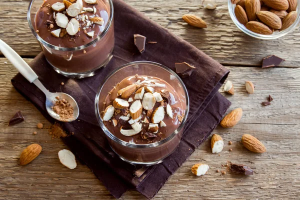 Healthy Raw Vegan Chocolate Mousse topped with Almond in glasses over wooden background close up - delicious homemade Raw Vegan Chocolate Pudding with Nuts and Carob powder