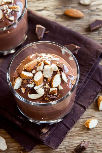 Healthy Raw Vegan Chocolate Mousse topped with Almond in glasses over wooden background close up - delicious homemade Raw Vegan Chocolate Pudding with Nuts and Carob powder