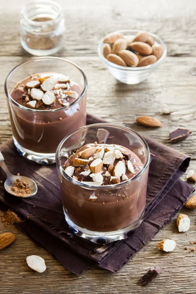 Çikolata Mousse ile badem ahşap arka plan üzerinde gözlük tepesinde yakın çekim - lezzetli ev yapımı çiğ Vegan çikolatalı puding ile fındık ve keçiboynuzu tozu