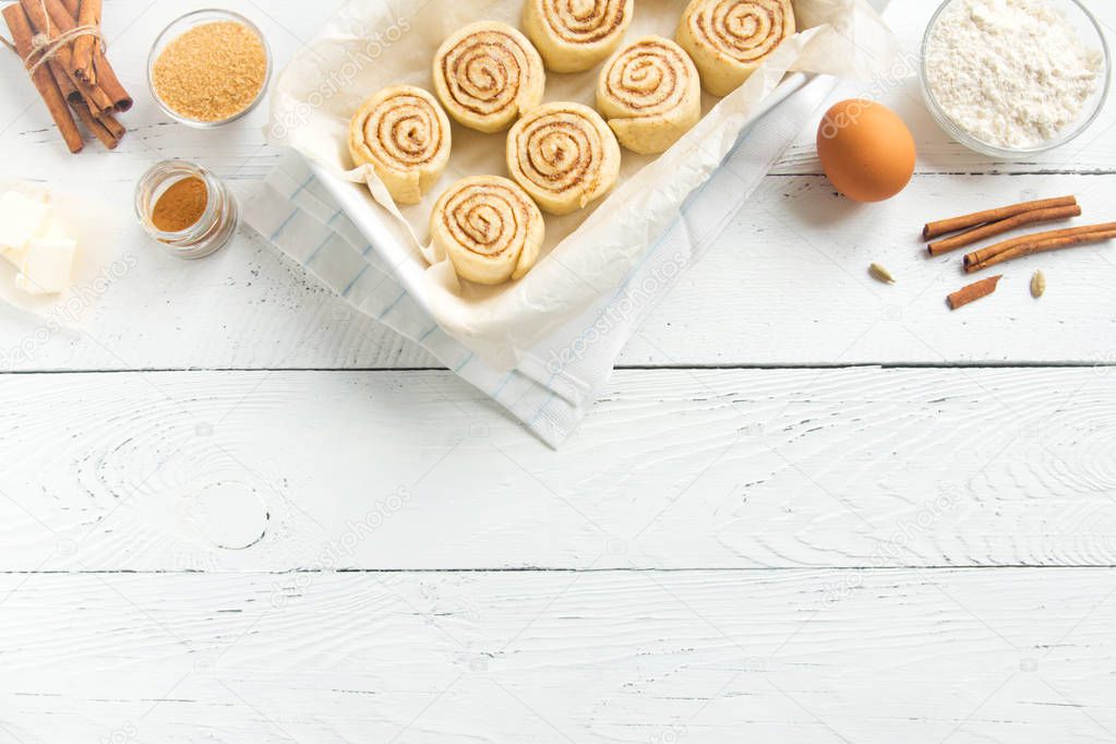 Cinnamon rolls or cinnabon, homemade recipe raw dough preparation sweet traditional dessert buns with pastry ingredients food on baking tray.