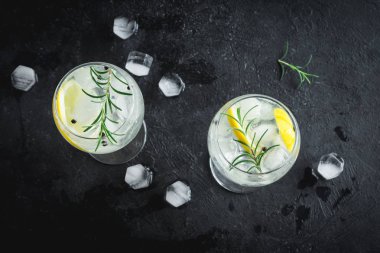 Alkol içki (cin tonik kokteyl) limon, biberiye ve rustik siyah taş tablo, kopya alanı, buza üst görünüm. Limon ve otlar ile buzlu içecek.