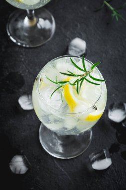 Alkol içki (cin tonik kokteyl) limon, biberiye ve rustik siyah taş tablo, kopya alanı, buza üst görünüm. Limon ve otlar ile buzlu içecek.