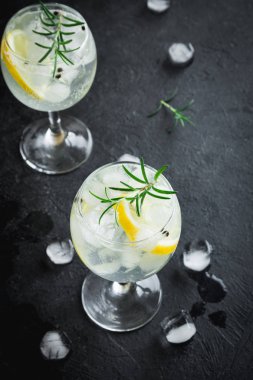 Alkol içki (cin tonik kokteyl) limon, biberiye ve rustik siyah taş tablo, kopya alanı, buza üst görünüm. Limonlu buzlu içecek.