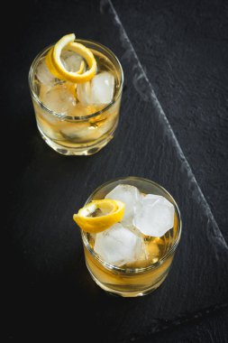 Limon kabuğu ile buzlu viski. Narenciye twist ile süslenmiş buzlu viski servis siyah taş zemin, üstten görünüm, kopya alanı.