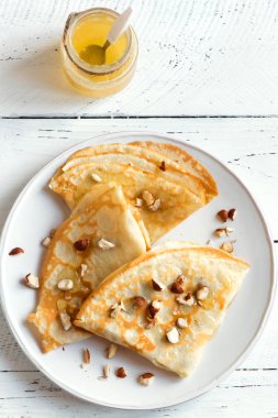 Krep Suzette bal ve fındık beyaz zemin üzerinde beyaz tabakta ile alanı kopyalayın. Kahvaltı için lezzetli ev yapımı krep.