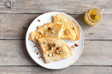 Krep Suzette bal ve fındık ahşap arka plan üzerinde beyaz tabakta ile alanı kopyalayın. Kahvaltı için lezzetli ev yapımı krep.