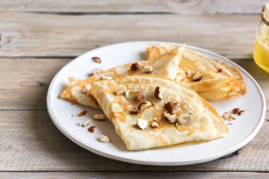 Krep Suzette bal ve fındık ahşap arka plan üzerinde beyaz tabakta ile alanı kopyalayın. Kahvaltı için lezzetli ev yapımı krep.