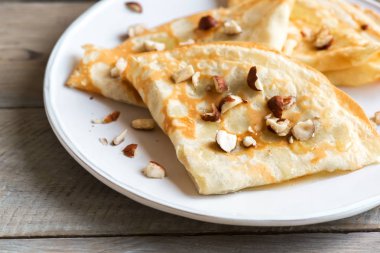 Krep Suzette bal ve fındık ahşap arka plan üzerinde beyaz tabakta ile alanı kopyalayın. Kahvaltı için lezzetli ev yapımı krep.