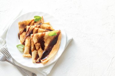 Çikolata sosu ve beyaz arka plan, kopya alanı üzerinde beyaz tabakta nane ile krep. Kahvaltı için lezzetli ev yapımı krep.