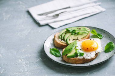 Sahanda yumurta - dilimlenmiş avokado ve roka için sağlıklı kahvaltı veya aperatif, kızarmış ekmek üzerinde yumurta ile avokado sandviç kopyalama alanı.