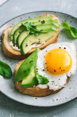 Sahanda yumurta - dilimlenmiş avokado ve sağlıklı kahvaltı veya aperatif için roka ile kızarmış ekmek üzerinde yumurta ile avokado sandviç.