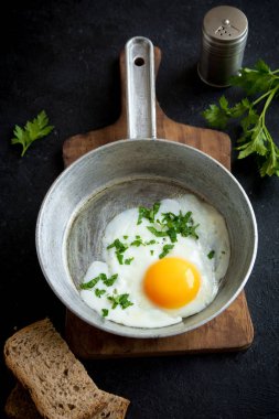 Kızartma tavası kahvaltıda kızarmış yumurta. Sahanda yumurta ekmek ve maydanoz üzerinde tava siyah taş tablo, üstten görünüm, kopya alanı.