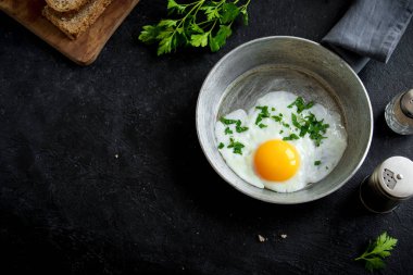 Kızartma tavası kahvaltıda kızarmış yumurta. Sahanda yumurta ekmek ve maydanoz üzerinde tava siyah taş tablo, üstten görünüm, kopya alanı.