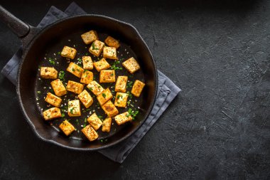 Susam ve baharat dökme demir tava, kopya alanı üzerinde Kızarmış tofu. Vegan vejetaryen diyet yemek yemek için sağlıklı bir madde. Siyah arka plan üzerine kavrulmuş soya peyniri.