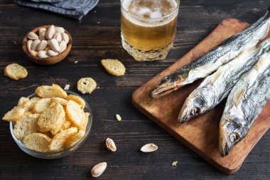 Çeşitli aperatifler bira için: güneş kurutulmuş balık, fındık, tuzlu kruton veya kraker ahşap arka plan, üstten görünüm üzerinden kopyalama alanı. Lager bira ve aperatifler, kurutulmuş smelts.