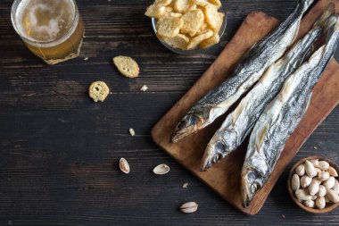 Çeşitli aperatifler bira için: güneş kurutulmuş balık, fındık, tuzlu kruton veya kraker ahşap arka plan, üstten görünüm üzerinden kopyalama alanı. Lager bira ve kurutulmuş gölde aperatifler.