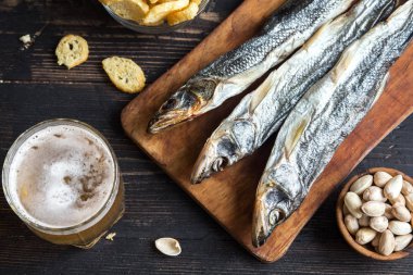 Assorted snacks for beer: sun dried fish, nuts, salted croutons or crackers and over wooden background, top view, copy space. Lager beer and snacks, dried smelts. clipart