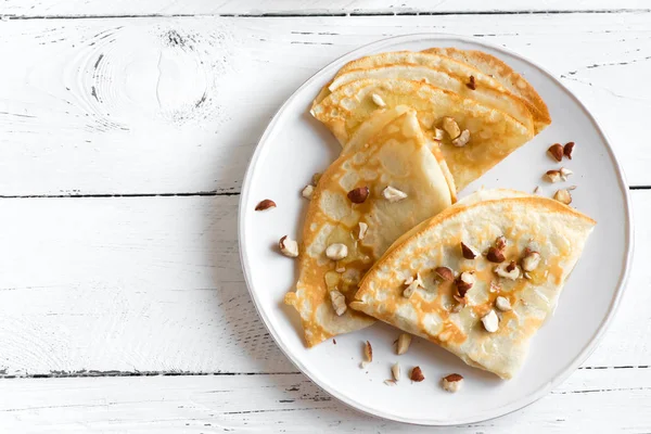 Krep Suzette bal ve fındık beyaz zemin üzerinde beyaz tabakta ile alanı kopyalayın. Kahvaltı için lezzetli ev yapımı krep.