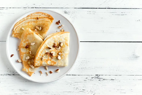 Krep Suzette bal ve fındık beyaz zemin üzerinde beyaz tabakta ile alanı kopyalayın. Kahvaltı için lezzetli ev yapımı krep.