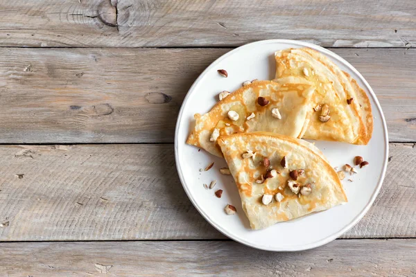 木製の背景上の白いプレート上のナッツと蜂蜜のクレープ シュゼット スペースにコピーします 朝食の美味しい自家製クレープ — ストック写真