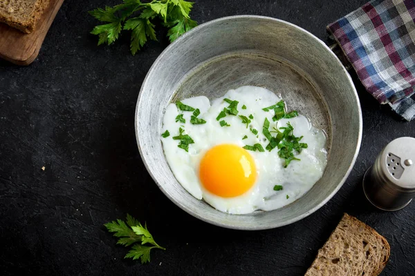 Kızartma tavası kahvaltıda kızarmış yumurta. Sahanda yumurta ekmek ve maydanoz üzerinde tava siyah taş tablo, üstten görünüm, kopya alanı.