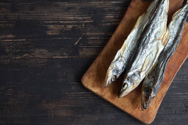 Sun dried fish, salted smelts over wooden background, top view, copy space. Snack  for beer dried smelts.