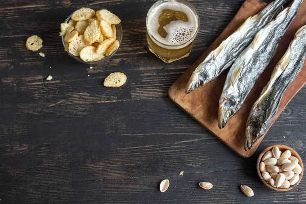 Çeşitli aperatifler bira için: güneş kurutulmuş balık, fındık, tuzlu kruton veya kraker ahşap arka plan, üstten görünüm üzerinden kopyalama alanı. Lager bira ve kurutulmuş gölde aperatifler.