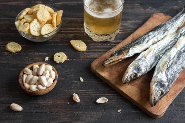 Çeşitli aperatifler bira için: güneş kurutulmuş balık, fındık, tuzlu kruton veya kraker ahşap arka plan, üstten görünüm üzerinden kopyalama alanı. Lager bira ve kurutulmuş gölde aperatifler.