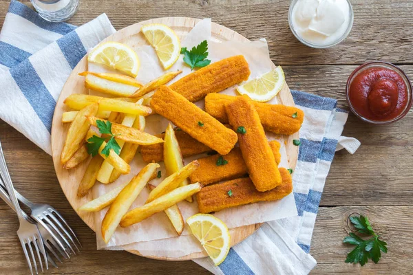 Fried Fish Sticks with French Fries. Fish Fingers over wooden background. Fish Sticks with fried potato and lemon ready to eat.