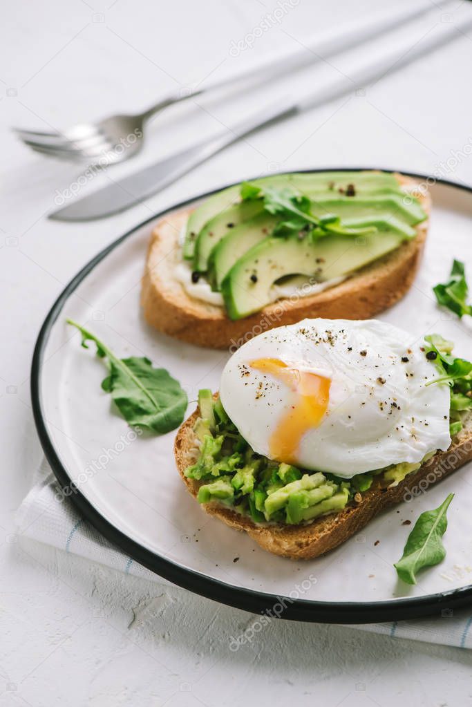 Avocado Sandwich with Poached Egg - sliced avocado and egg on toasted bread for healthy breakfast or snack, copy space.