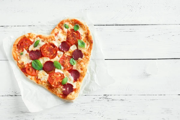 Heart shaped pizza over wooden background with copy space. Pizza with tomatoes, pepperoni, mozzarella cheese and basil for Valentine\'s day.