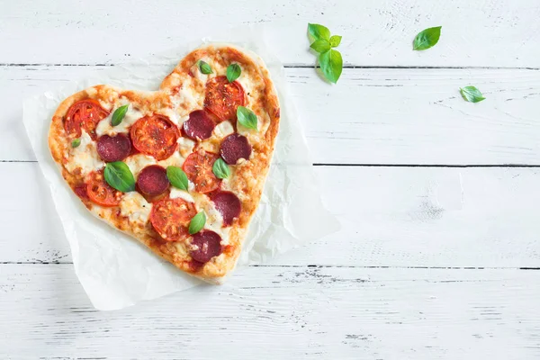 Kalp kopya alanı ile ahşap arka plan üzerinde pizza şeklinde. Pizza domates, biber, mozzarella peyniri ve Sevgililer günü için fesleğen ile.