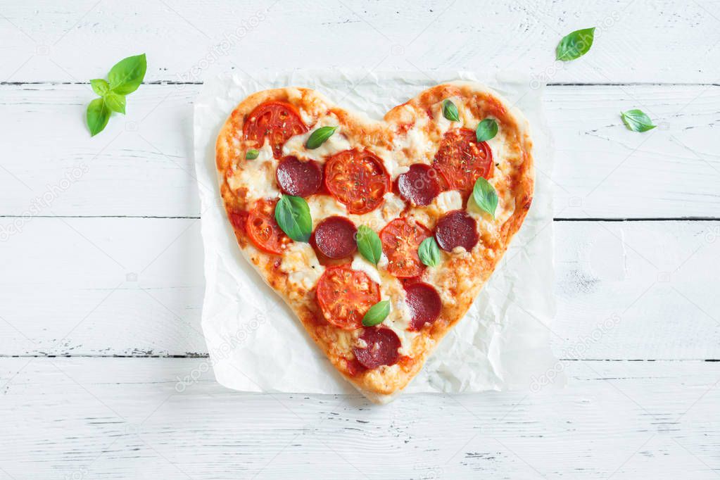 Heart shaped pizza over wooden background with copy space. Pizza with tomatoes, pepperoni, mozzarella cheese and basil for Valentine's day.