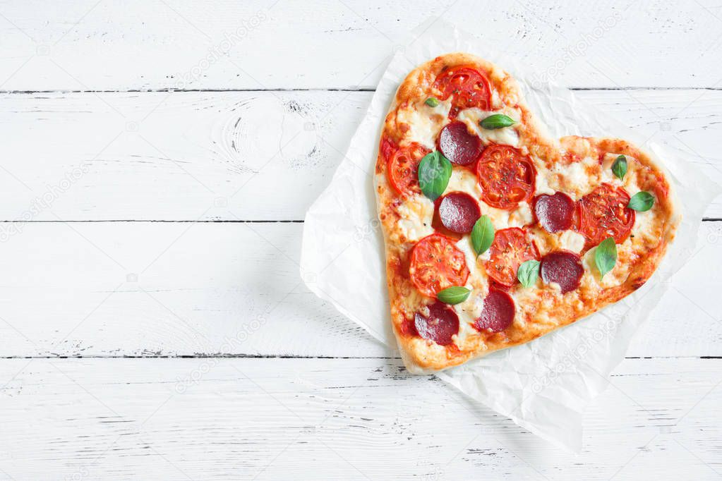 Heart shaped pizza over wooden background with copy space. Pizza with tomatoes, pepperoni, mozzarella cheese and basil for Valentine's day.