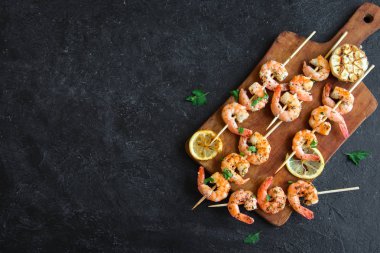 Izgara karides şişi. Deniz ürünleri, kabuklu deniz ürünleri. Karidesli karides şiş, otlu, sarımsaklı ve limonlu, siyah taşlı arka plan, kopyalama alanı. Karides, karides, esmer kebap. Barbekü karidesleri..