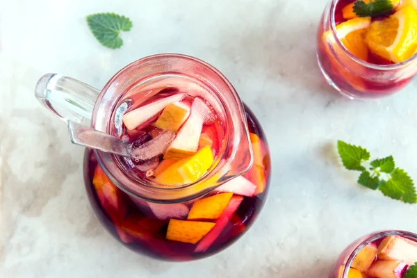 Red wine sangria or punch with fruits and ice in glasses and pincher. Homemade refreshing fruit sangria over rustic wooden table, copy space