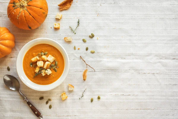 Pumpkin soup and organic pumpkins, top view, copy space. Seasonal autumn food - Spicy pumpkin soup with croutons and pumpkin seeds.