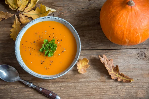 Pumpkin soup and organic pumpkins on wooden table. Seasonal autumn food - Spicy pumpkin soup in bowl.