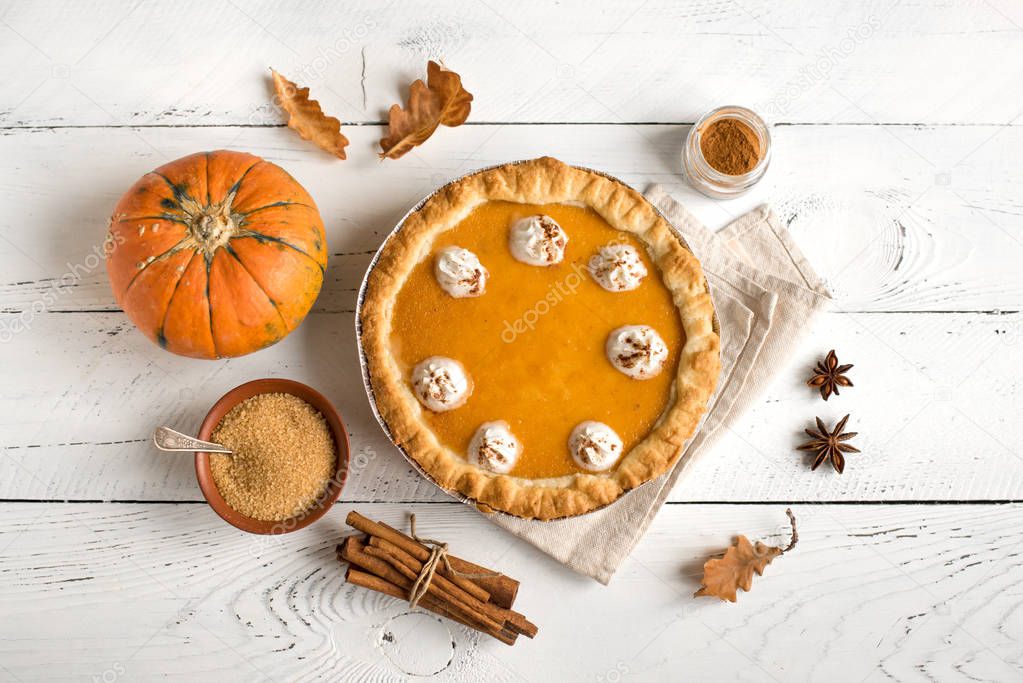 Pumpkin Pie with whipped cream and cinnamon on white wooden background, top view. Homemade pastry for Thanksgiving traditional Pumpkin Pie.
